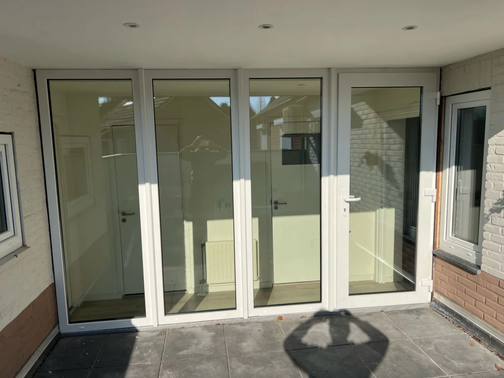 Moderne ruimte met witte glazen deuren, klein raam, betegelde vloer en radiator aan lichte muur